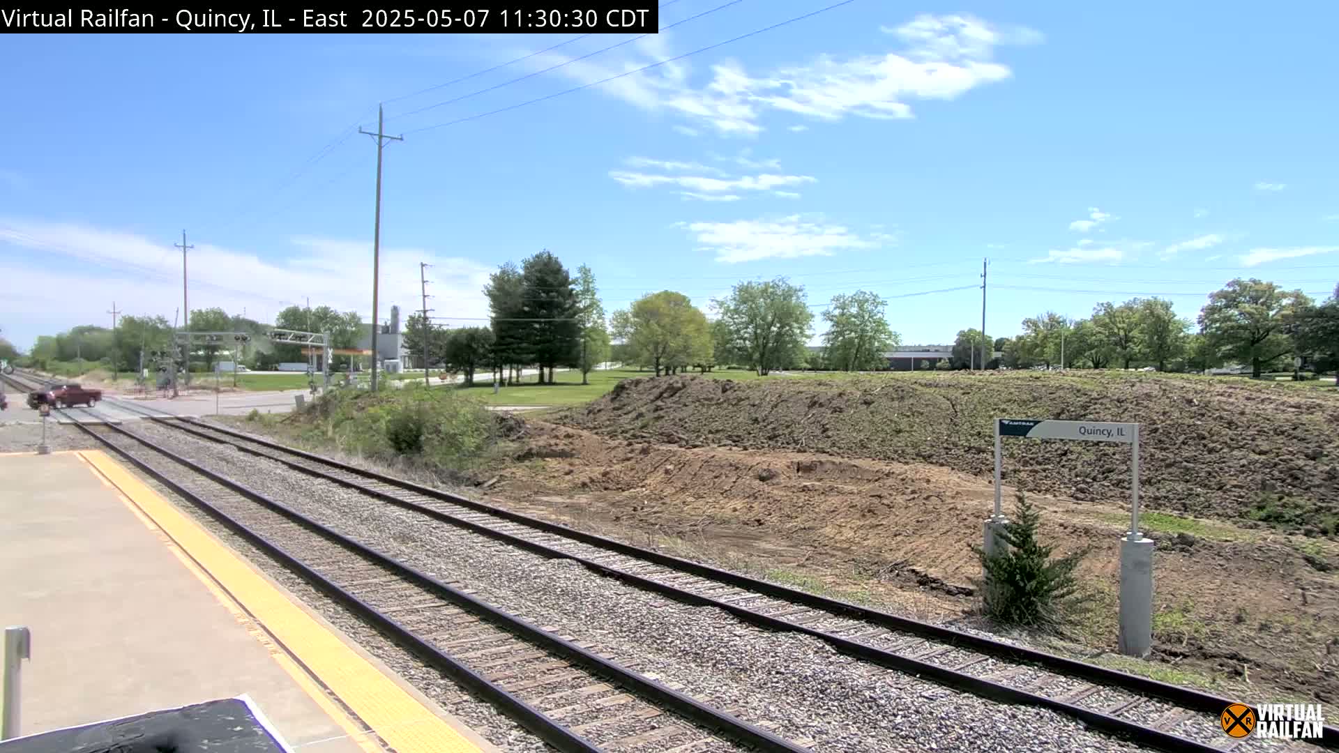 A train track with a partly sunny sky and a pile of dirt beside it.