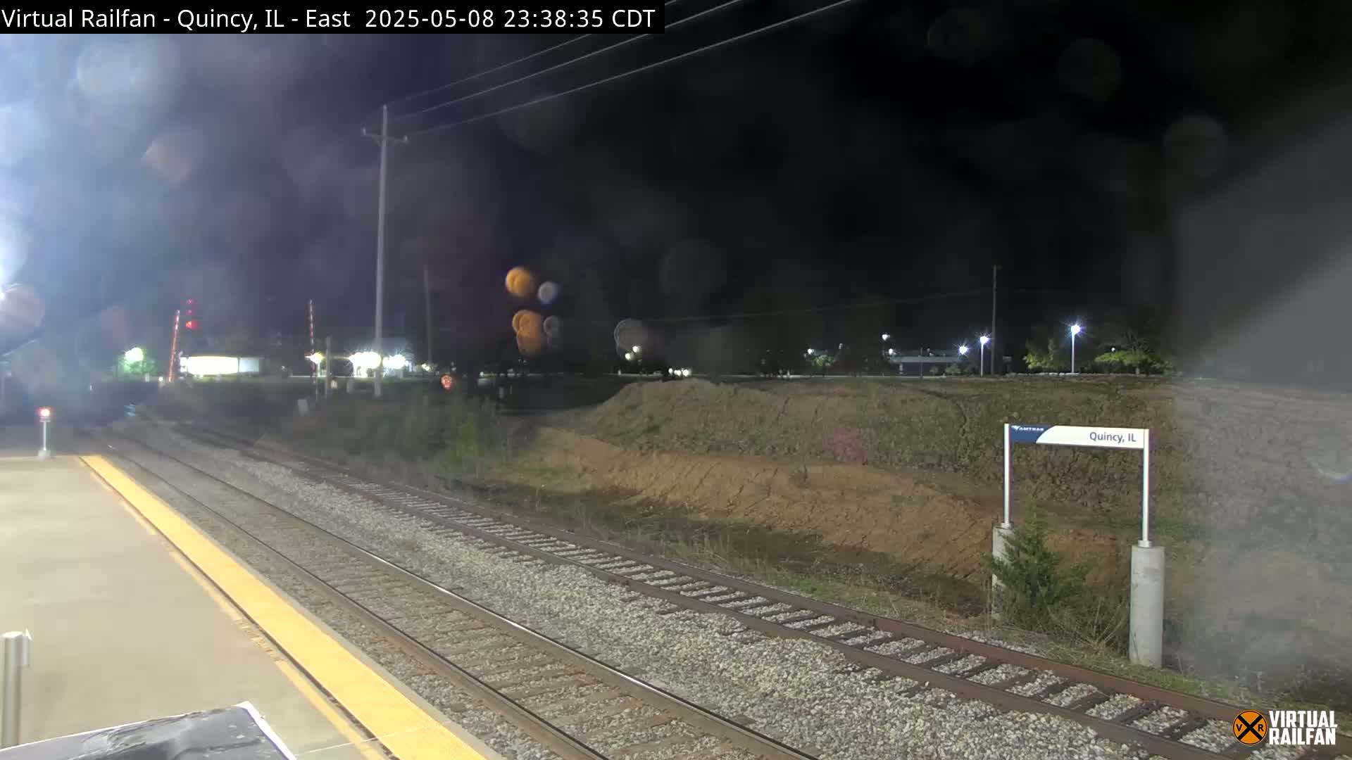A nighttime view of train tracks at a station, with a slightly hazy or foggy atmosphere.
