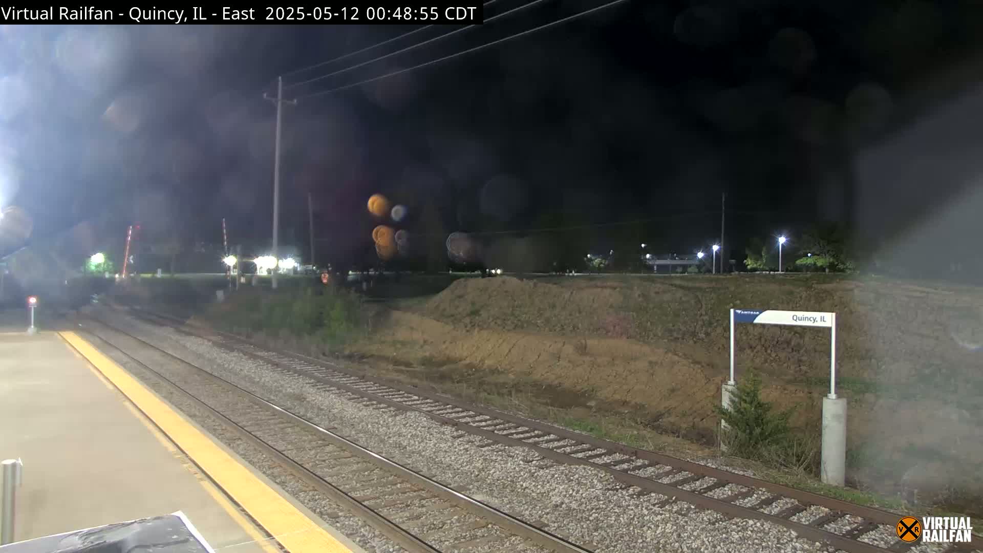 A nighttime view of train tracks at a station, with a slightly hazy or foggy atmosphere.