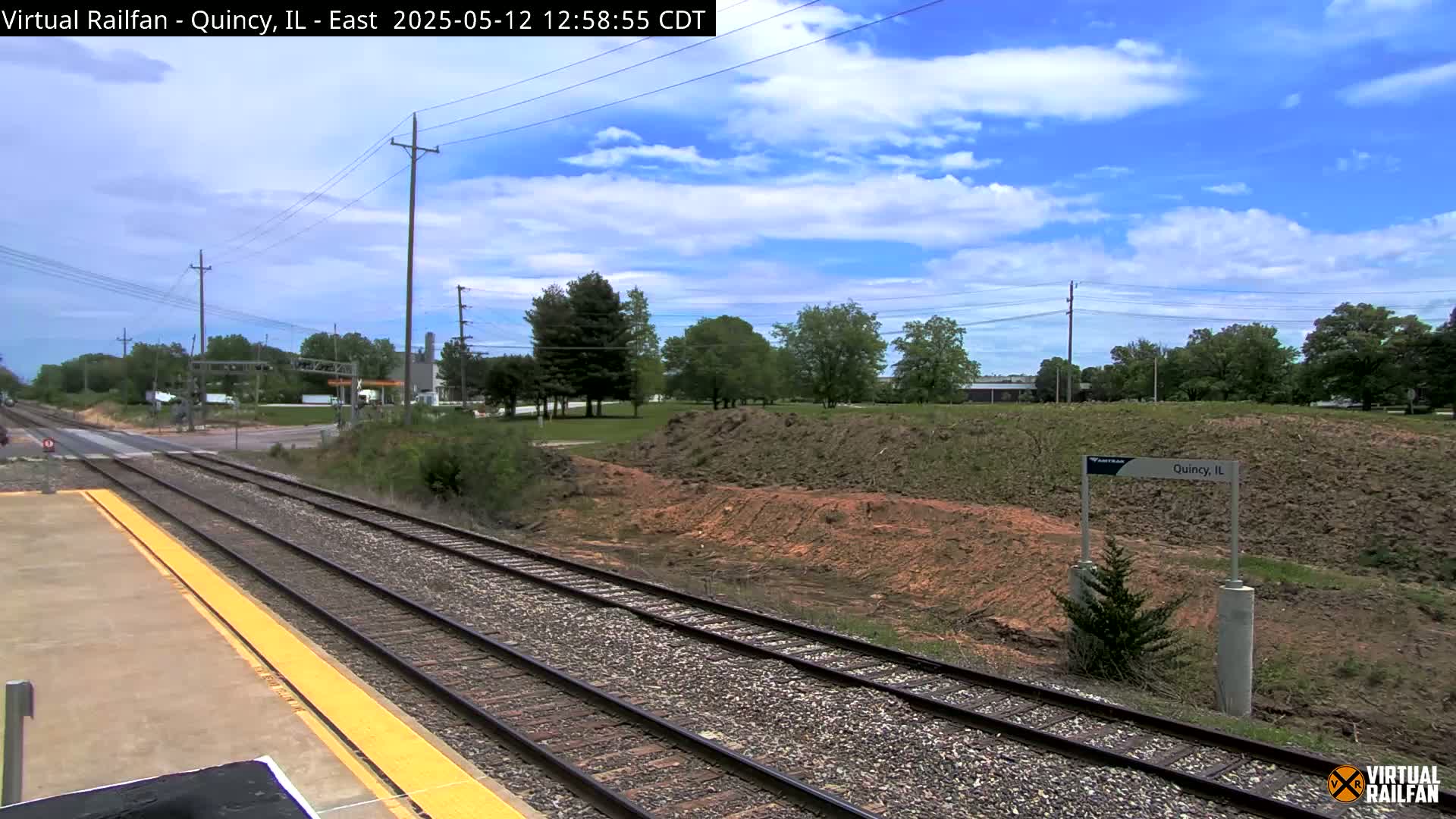 Train tracks extend into the distance under a partly cloudy blue sky, with a small amount of earthworks visible beside the tracks.