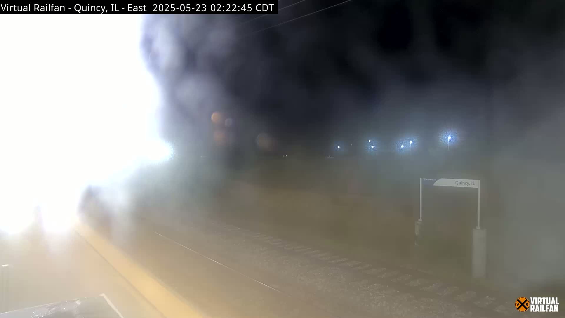 A nighttime, foggy view of a train platform with a train partially obscured by fog and steam.