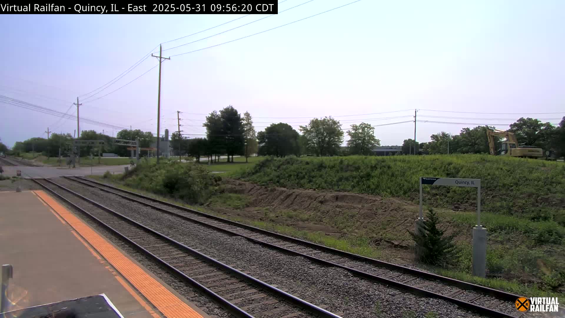 A view of train tracks at a station on a partly cloudy day, with some construction visible in the background.