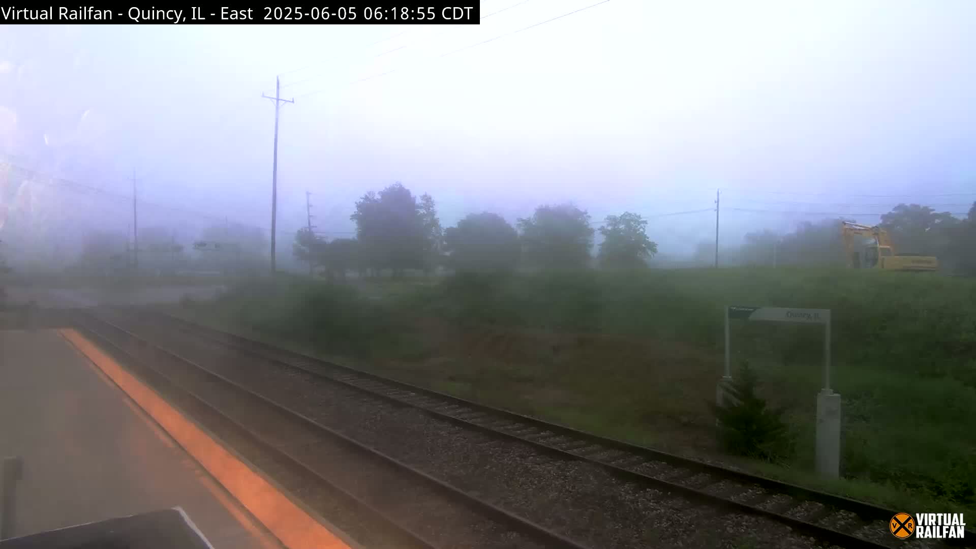 A foggy view from a train shows a railway track leading into a misty landscape with trees and a piece of heavy machinery.