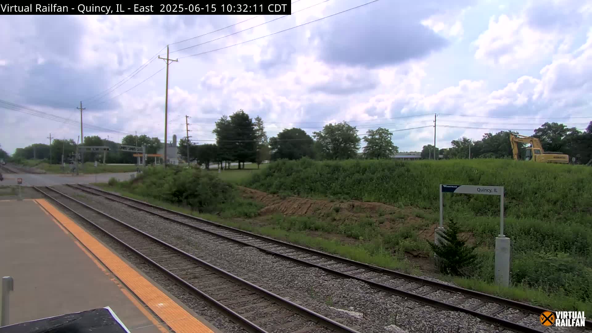 A view of train tracks at a station on an overcast day, with some construction equipment visible in the distance.