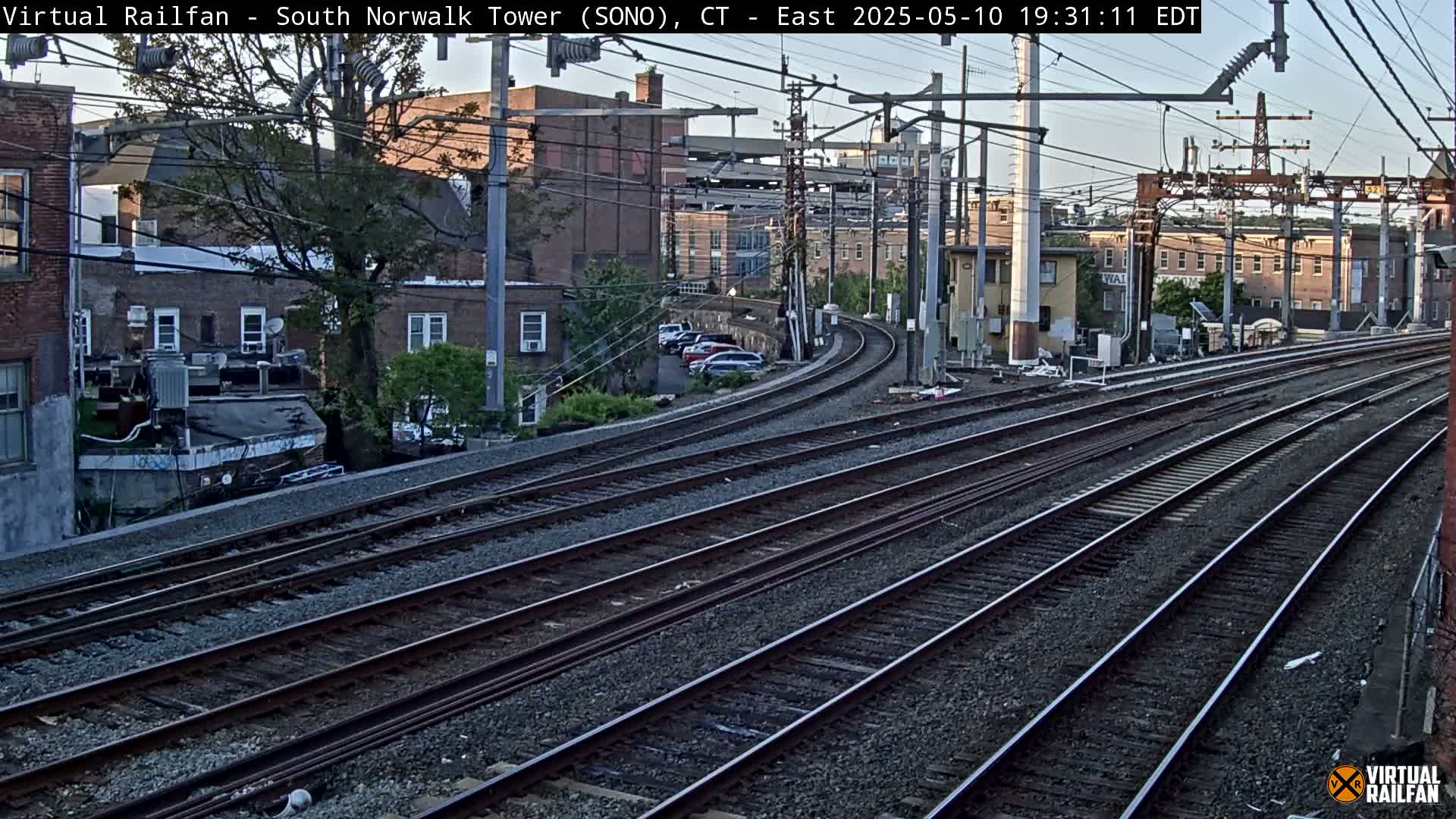 Multiple train tracks curve gently through a residential area under a twilight sky.