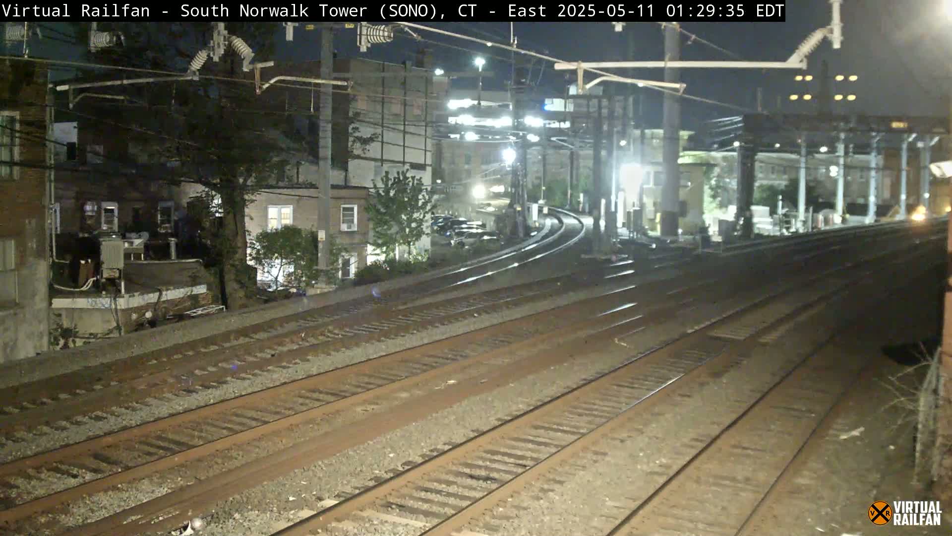 At night, several sets of train tracks curve toward a dimly lit residential area.