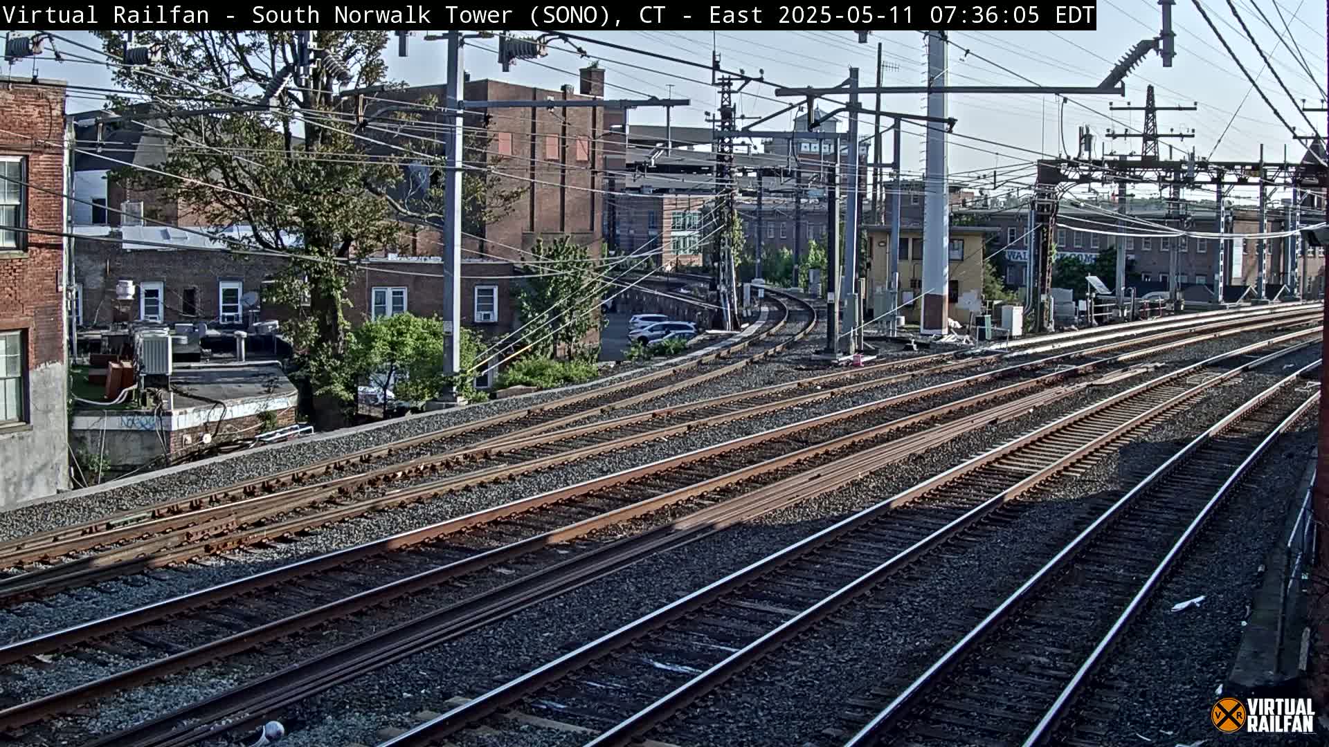 Multiple train tracks curve through a cityscape under a partly sunny sky.