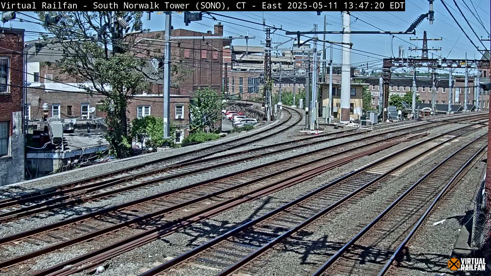 Multiple sets of train tracks curve through a city neighborhood under a sunny sky.