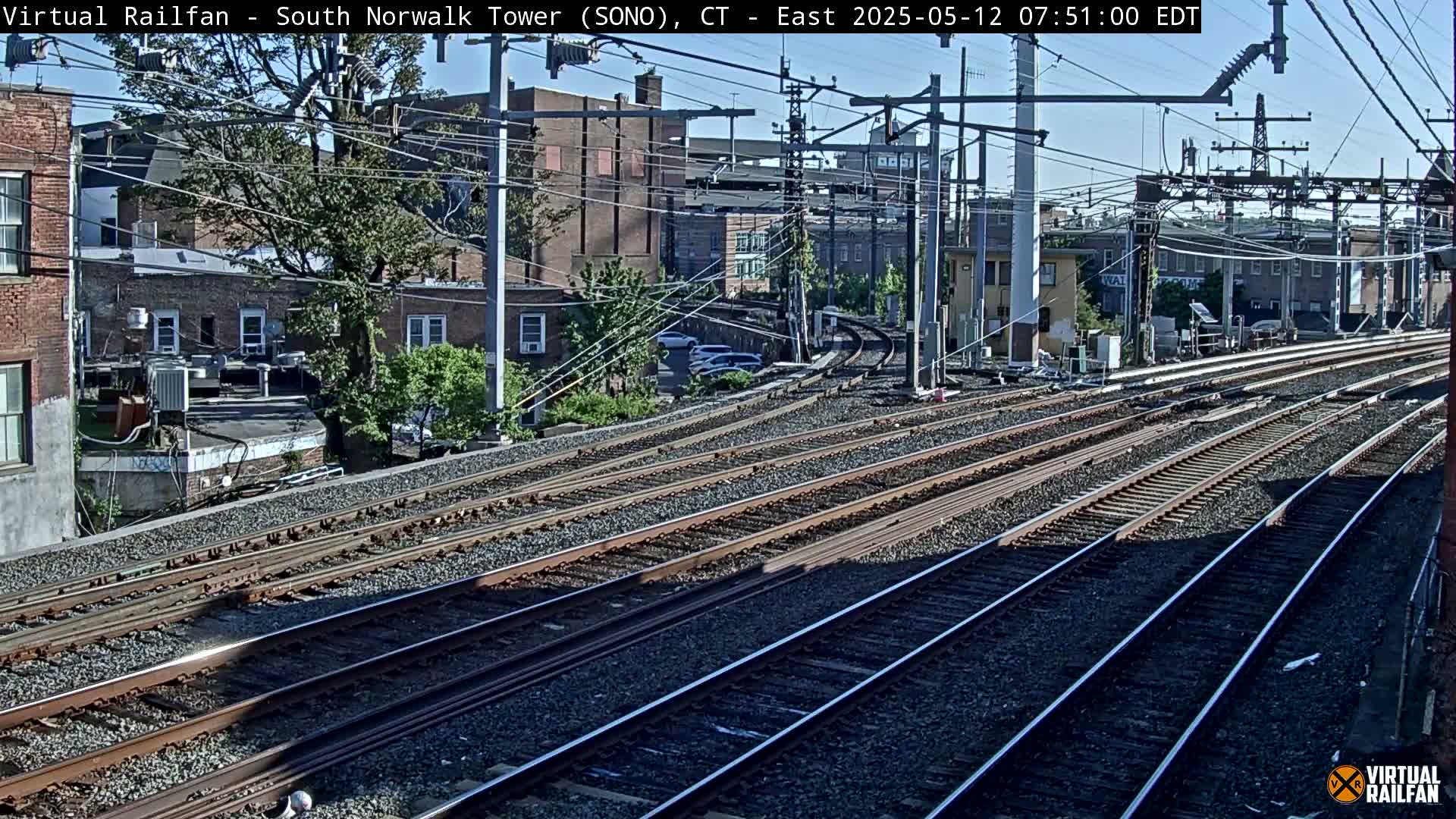 Multiple train tracks curve through a residential area on a sunny day.