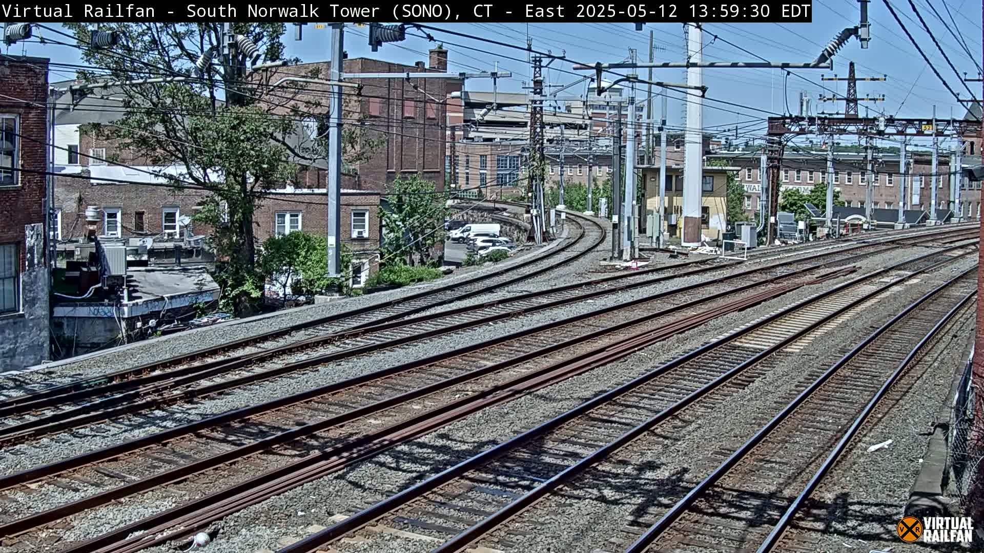 Several sets of train tracks curve away from the viewer towards buildings under a sunny sky.