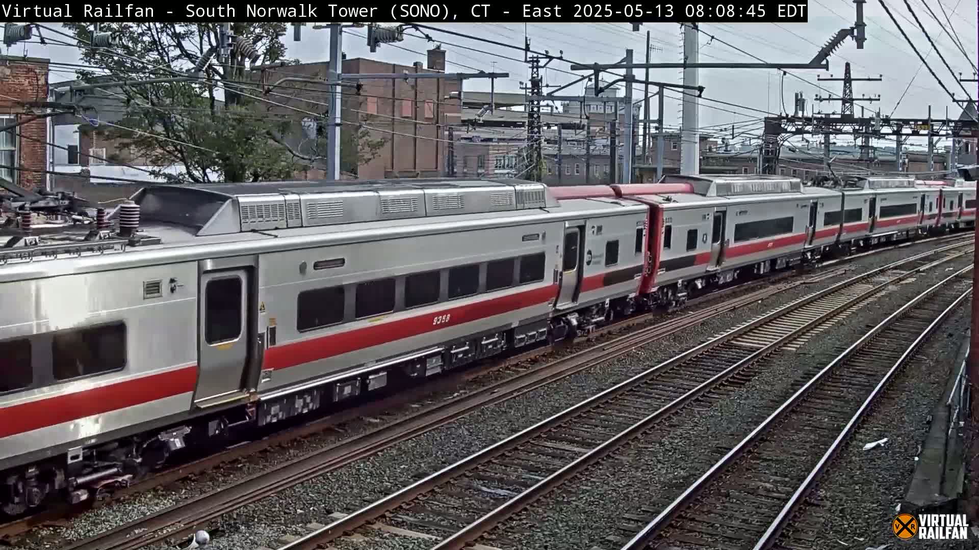 A long silver and red passenger train travels along multiple train tracks on an overcast day.
