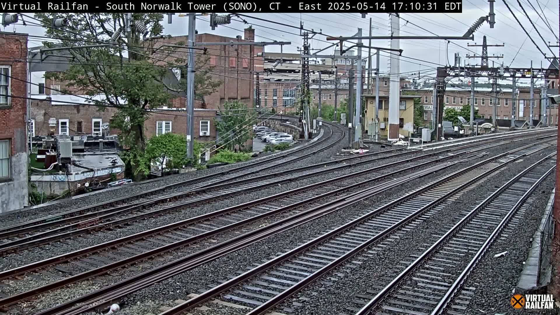 Multiple train tracks curve gently through an urban area under an overcast sky.