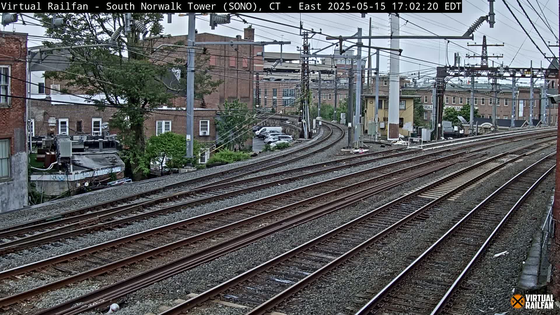 Several sets of train tracks curve gently through an urban area under an overcast sky.