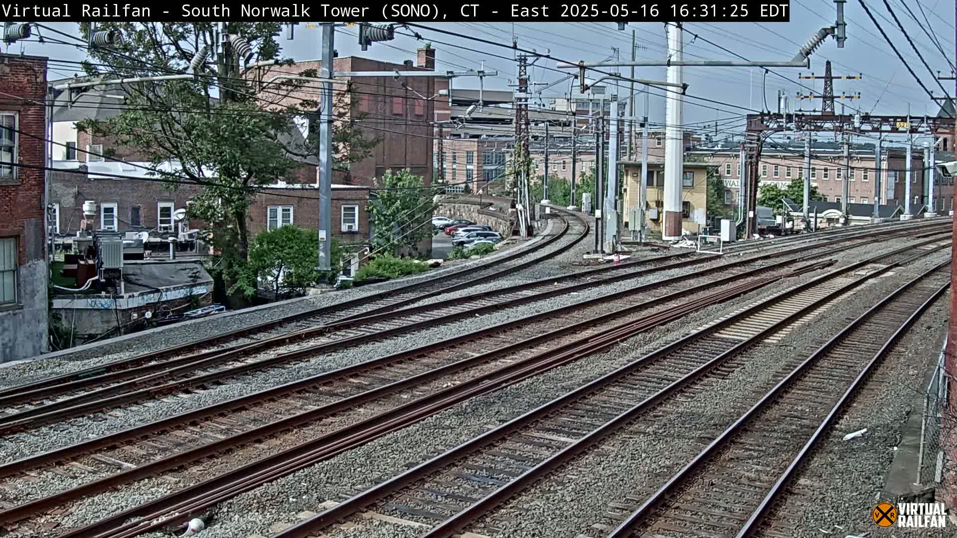 Multiple train tracks curve gently through a cityscape under a partly cloudy sky.