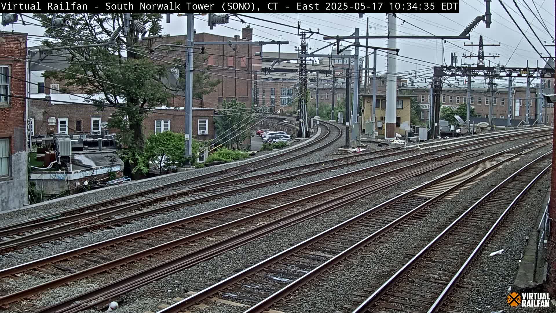 Several sets of train tracks curve gently through an urban area under an overcast sky.