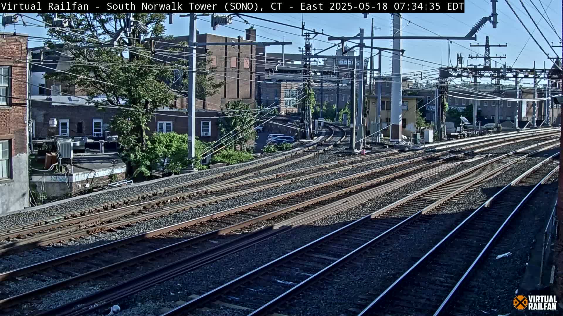 Several sets of train tracks curve through a city neighborhood on a partly sunny day.