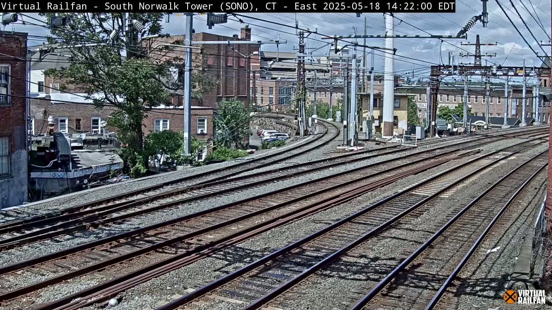 Multiple train tracks curve gently through a cityscape under a partly cloudy sky.