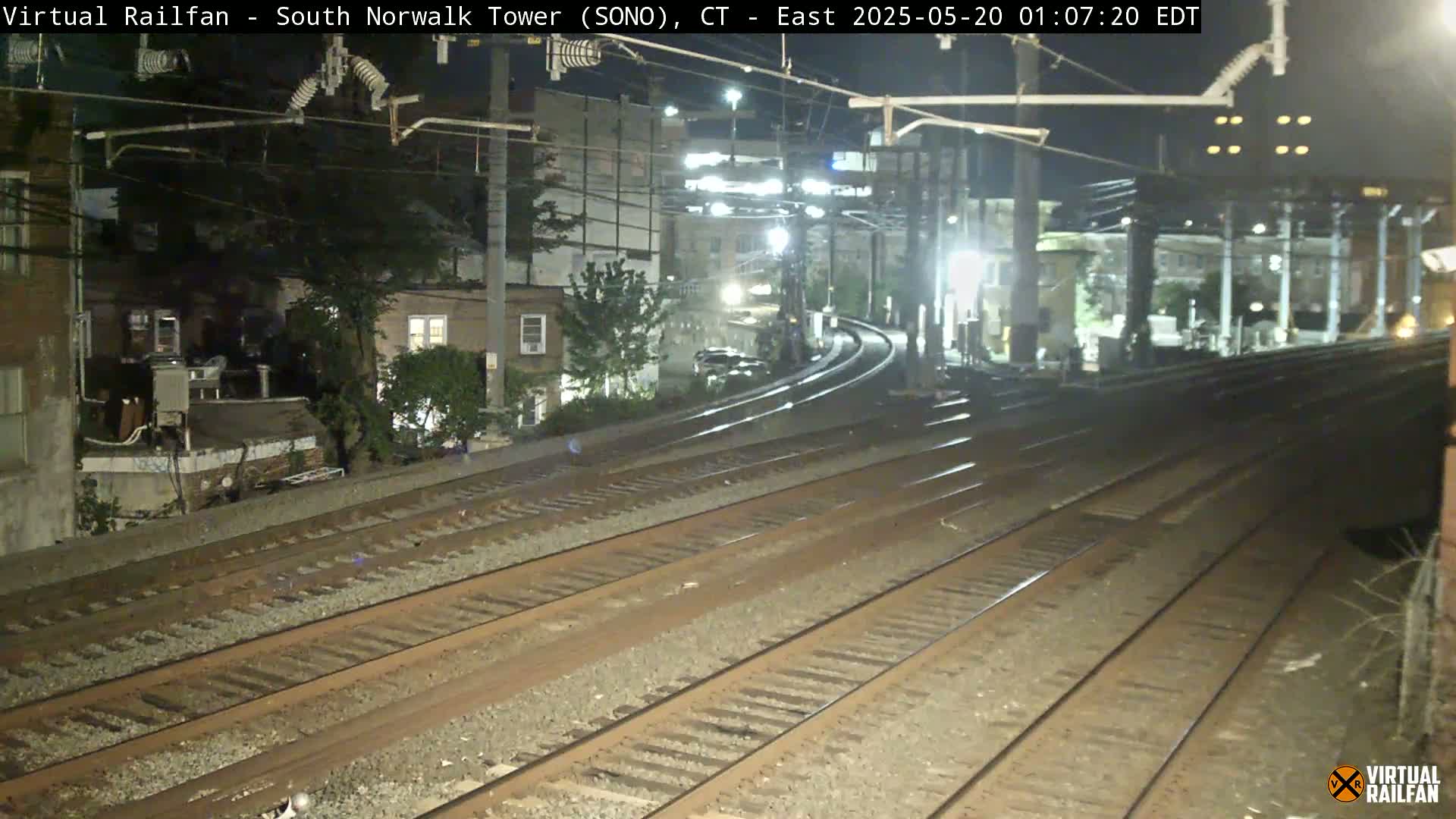 Several sets of train tracks at night, curving toward buildings and trees under illuminated streetlights.