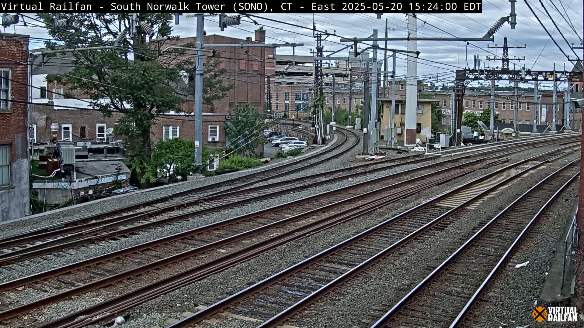Multiple sets of train tracks curve gently through an urban area under an overcast sky.