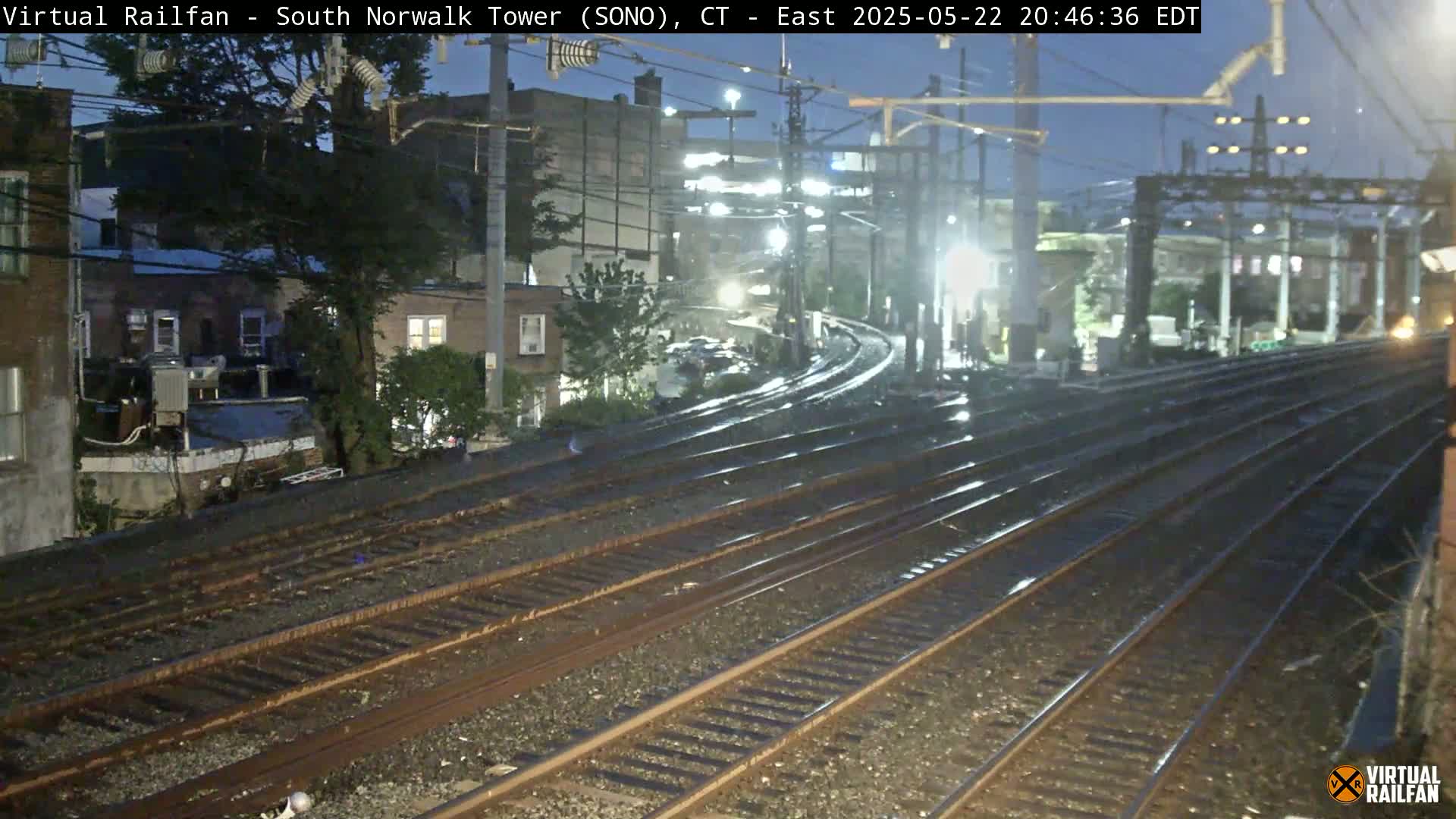 Wet train tracks curve through a nighttime cityscape under a dark sky.