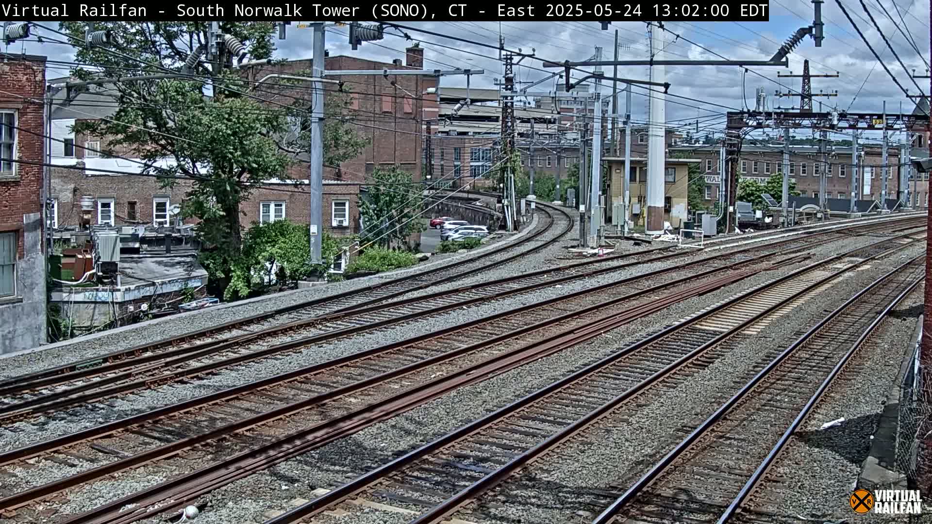 Multiple train tracks curve gently through a cityscape under a partly cloudy sky.