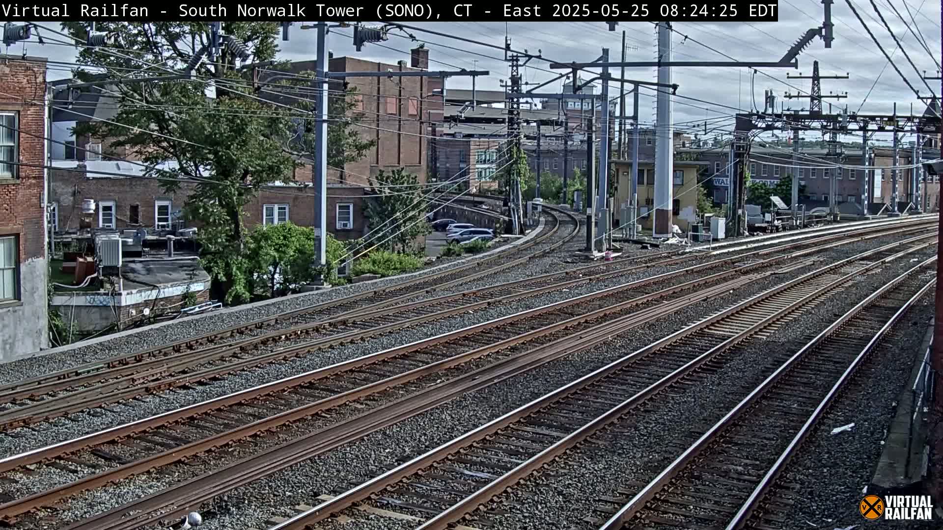 Multiple train tracks curve gently through a city under a partly cloudy sky.