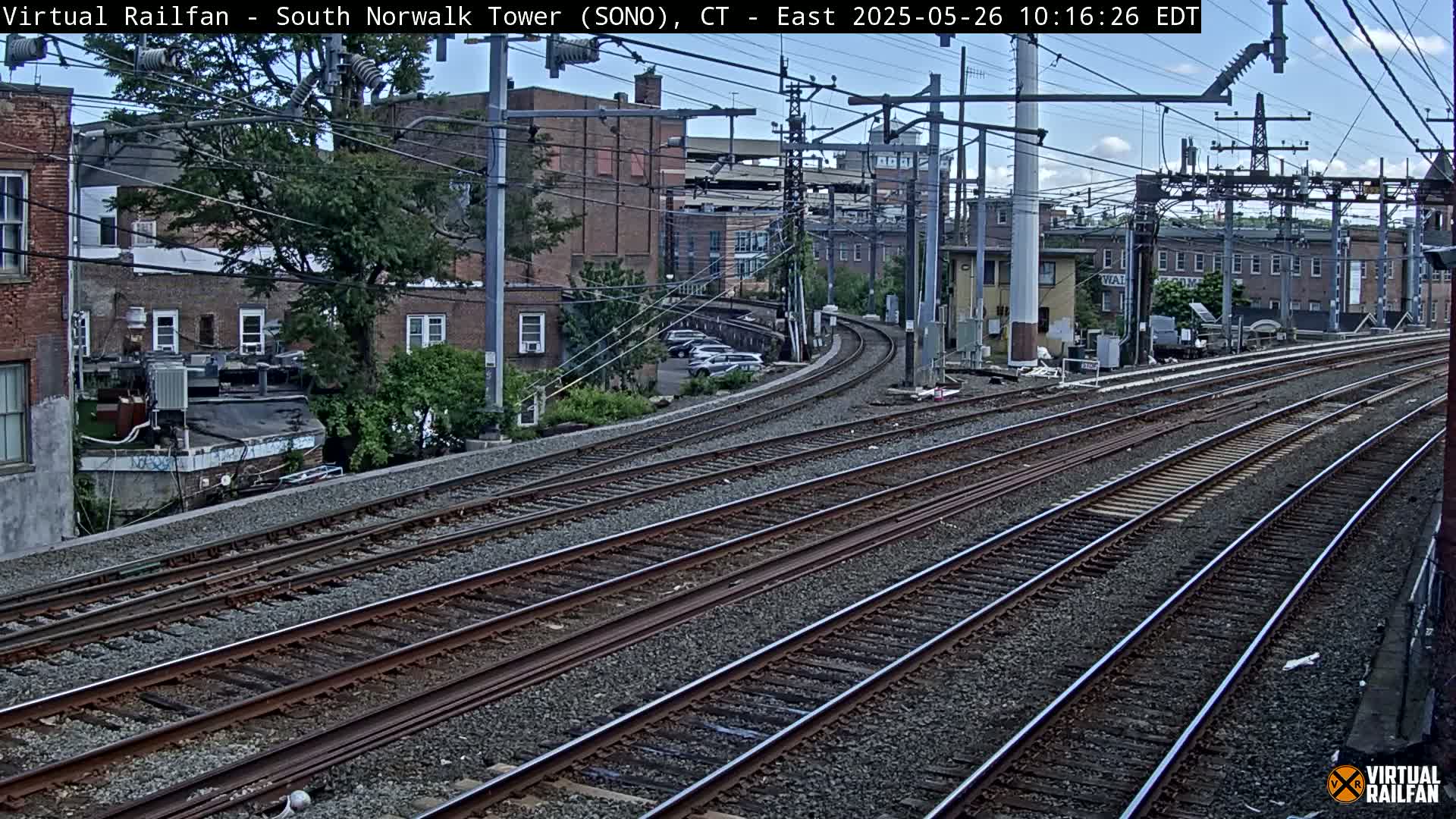 Multiple train tracks curve through a city neighborhood under a partly cloudy sky.