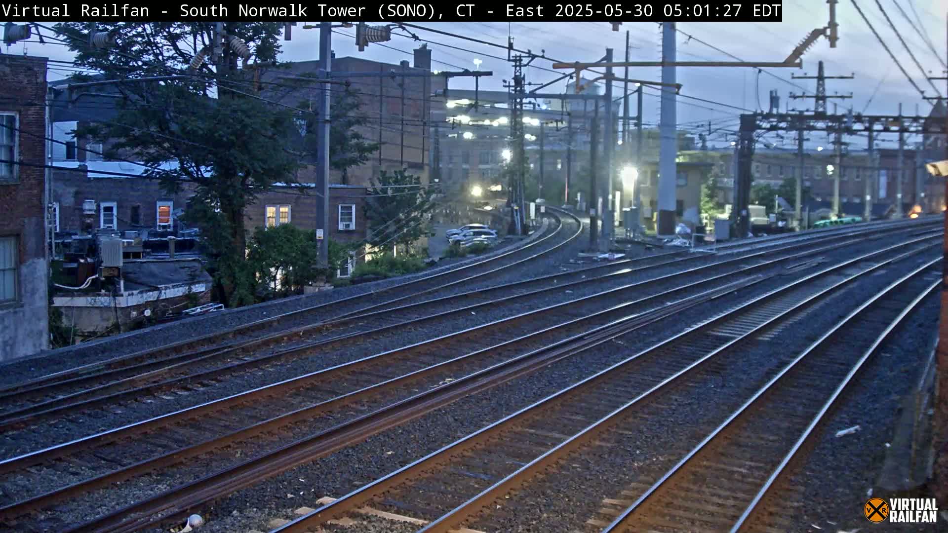 Multiple train tracks curve away from the camera toward buildings under a twilight sky.