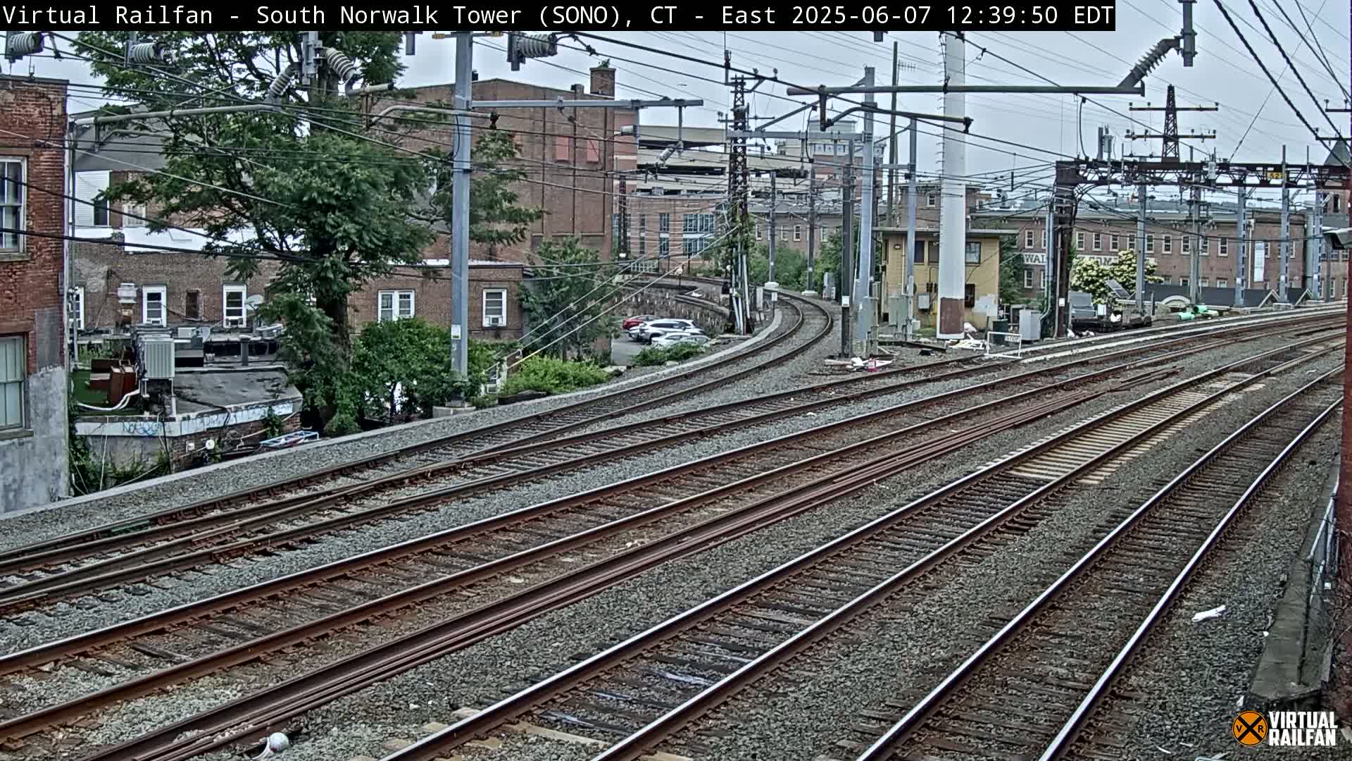 Multiple sets of train tracks curve gently around buildings under an overcast sky.