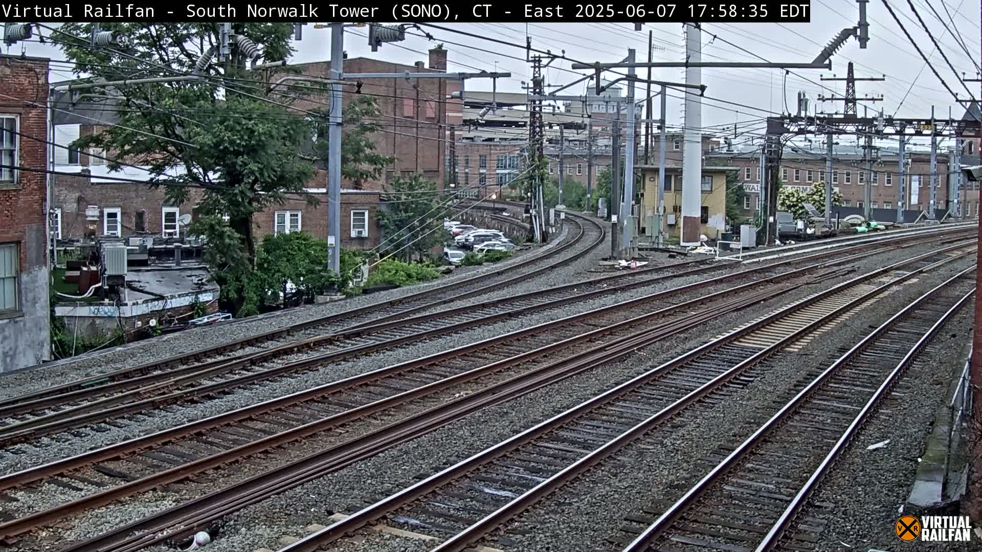 Multiple train tracks curve through a city neighborhood on an overcast day.