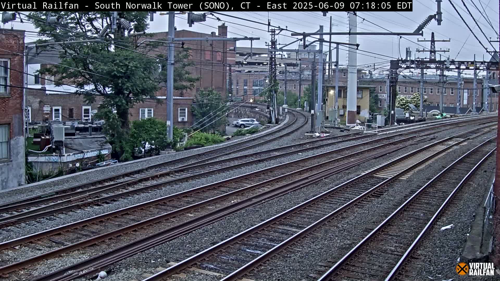 Multiple train tracks curve through an urban area under an overcast sky.