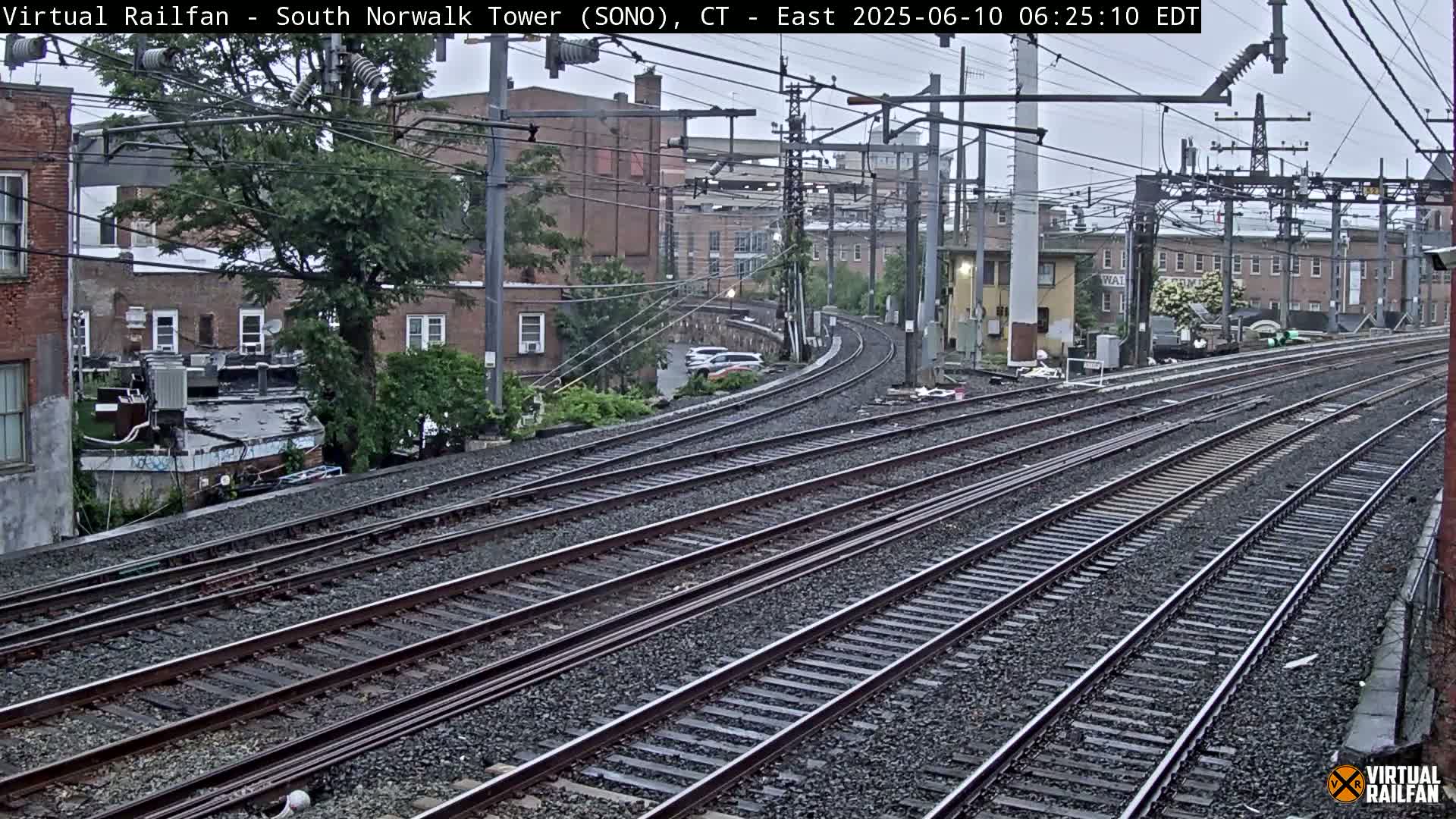Multiple train tracks curve through an urban area on an overcast day.