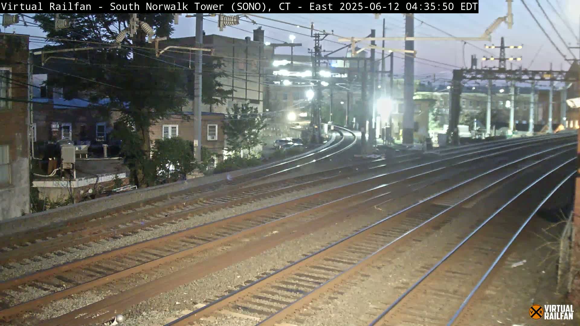 Multiple sets of train tracks curve toward a dimly lit urban area under a twilight sky.