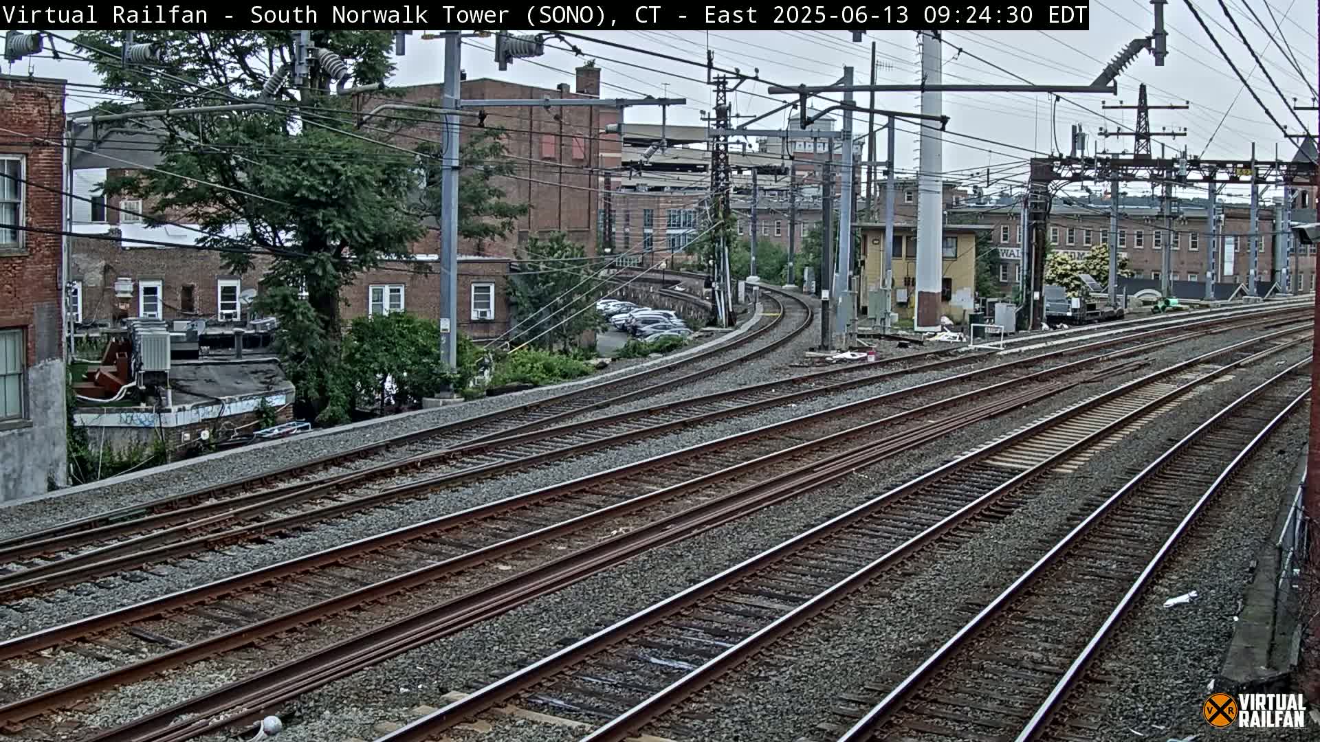 Multiple train tracks curve gently around brick buildings under an overcast sky.