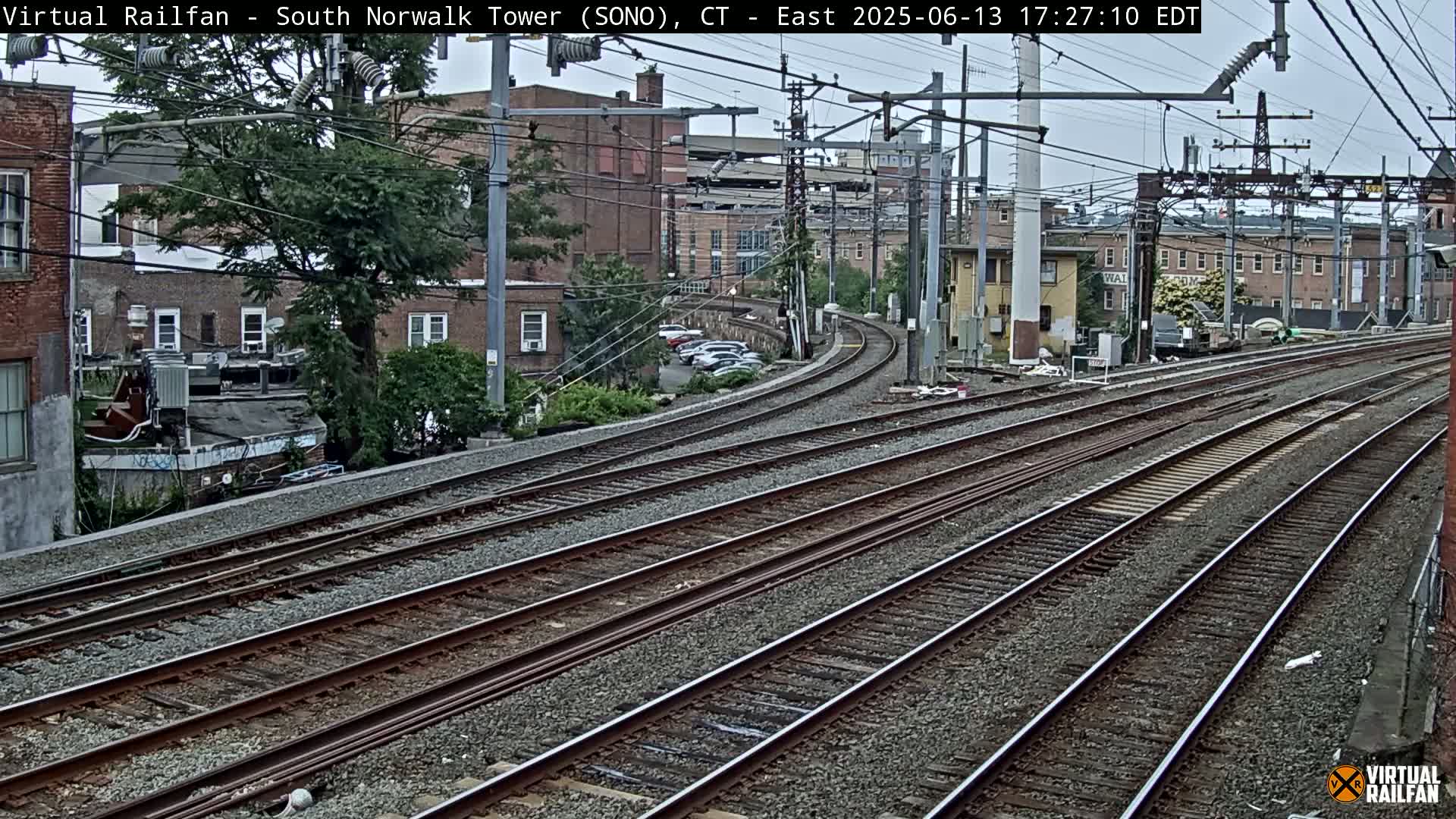 Multiple train tracks curve through a city neighborhood under an overcast sky.