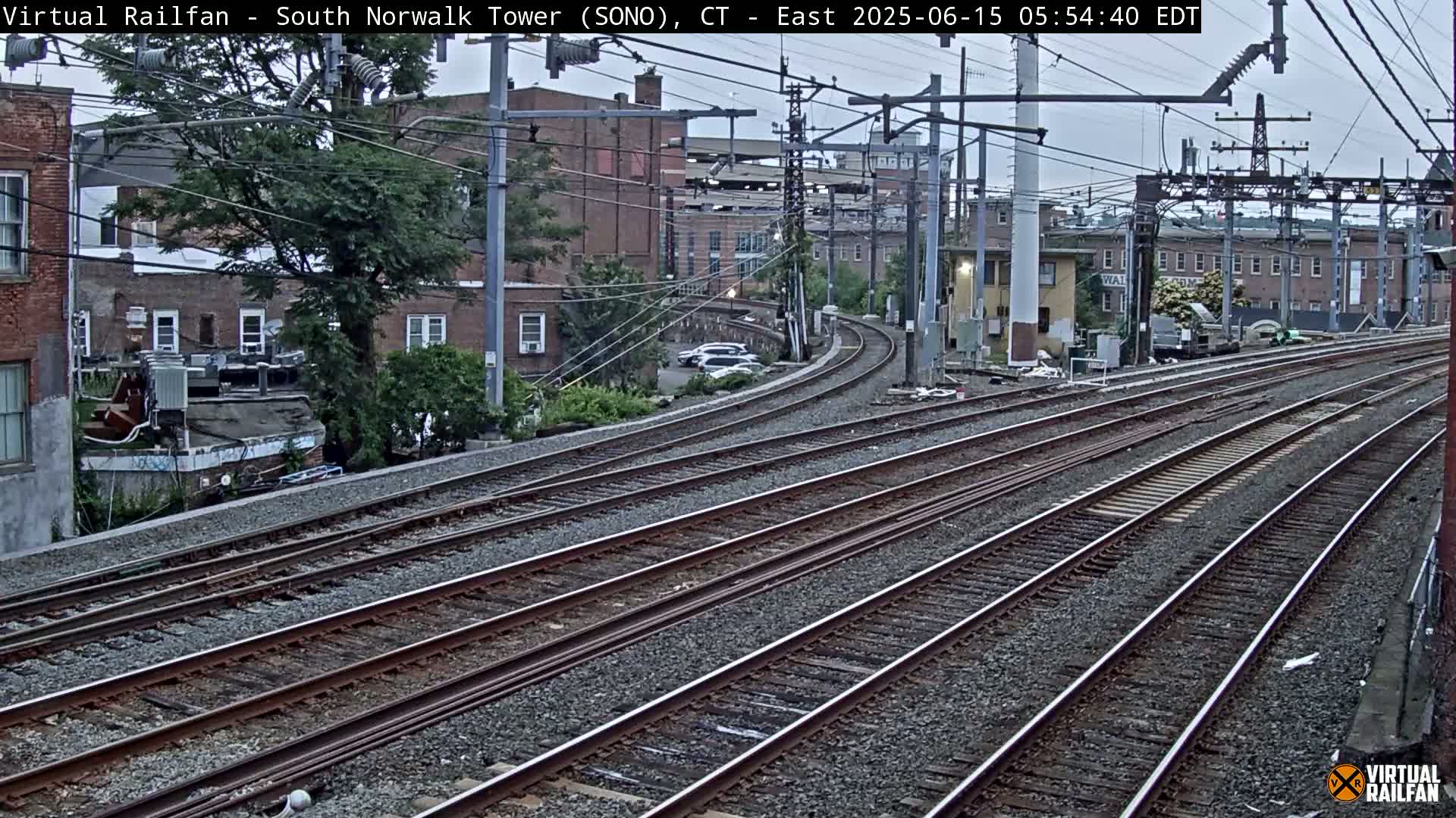 Multiple train tracks curve around buildings under an overcast sky.