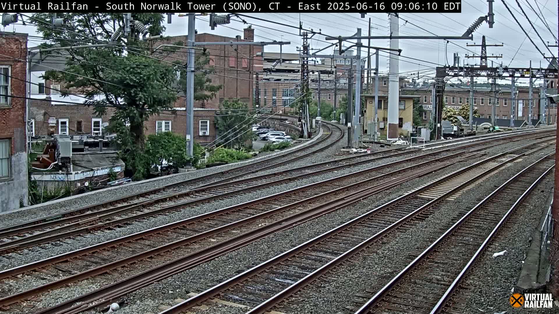 Multiple sets of train tracks curve gently through an urban area on an overcast day.