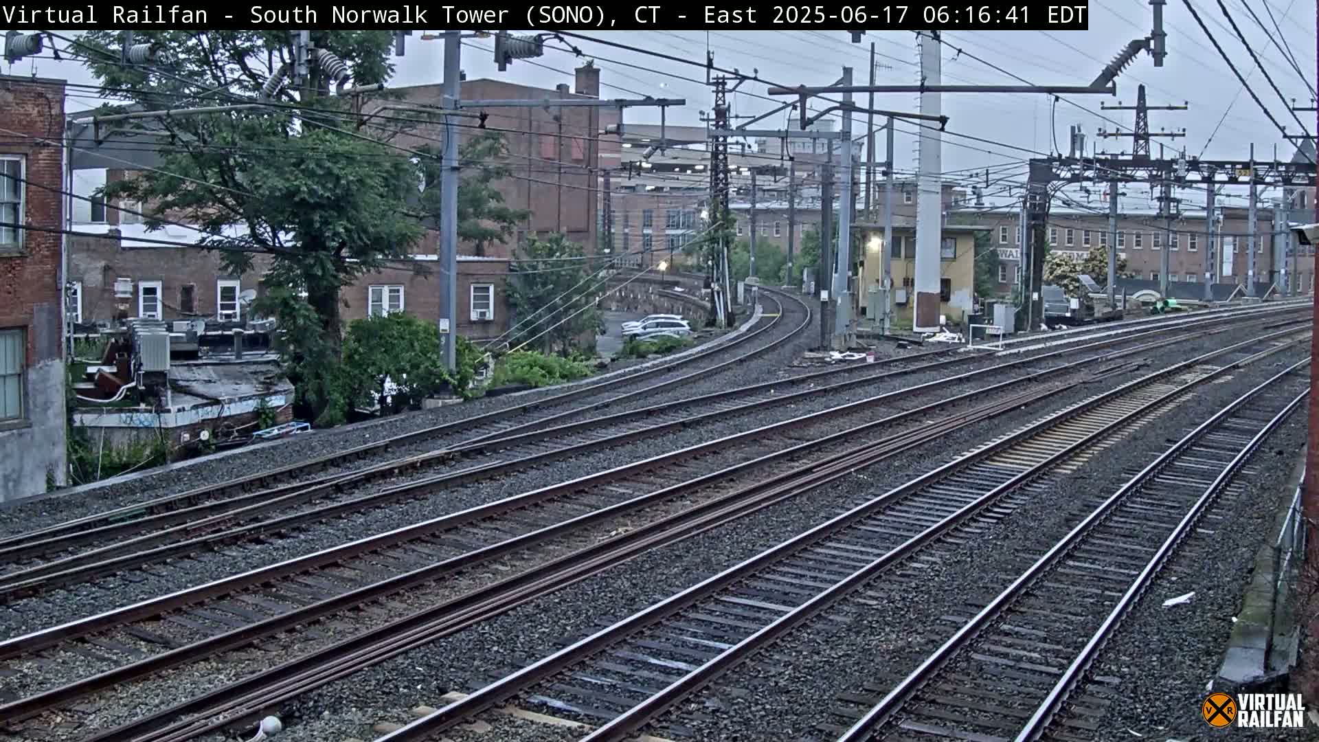 Multiple sets of train tracks curve gently through an urban area under an overcast sky.
