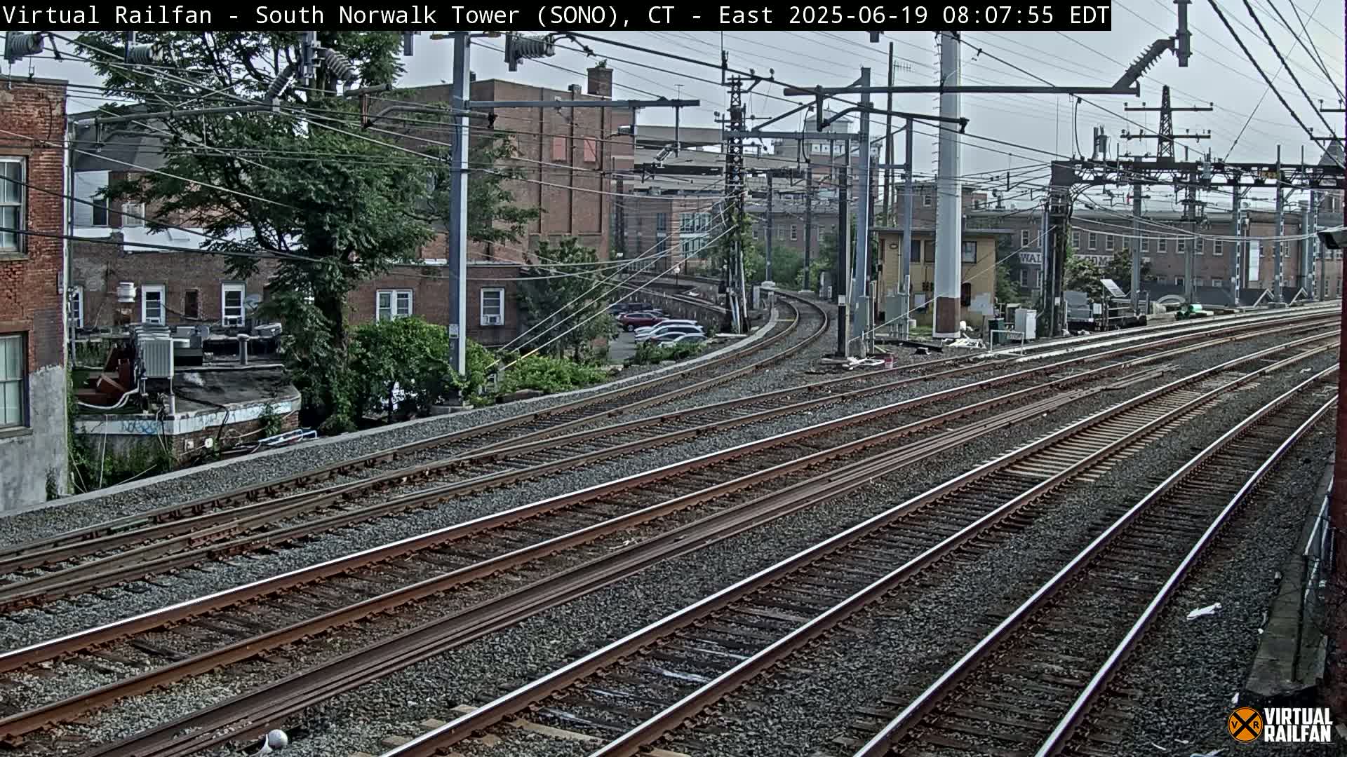 Multiple sets of train tracks curve gently around buildings on an overcast day.