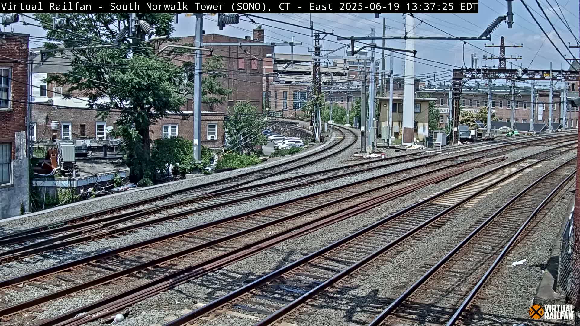 Multiple train tracks curve through a city on a partly sunny day.