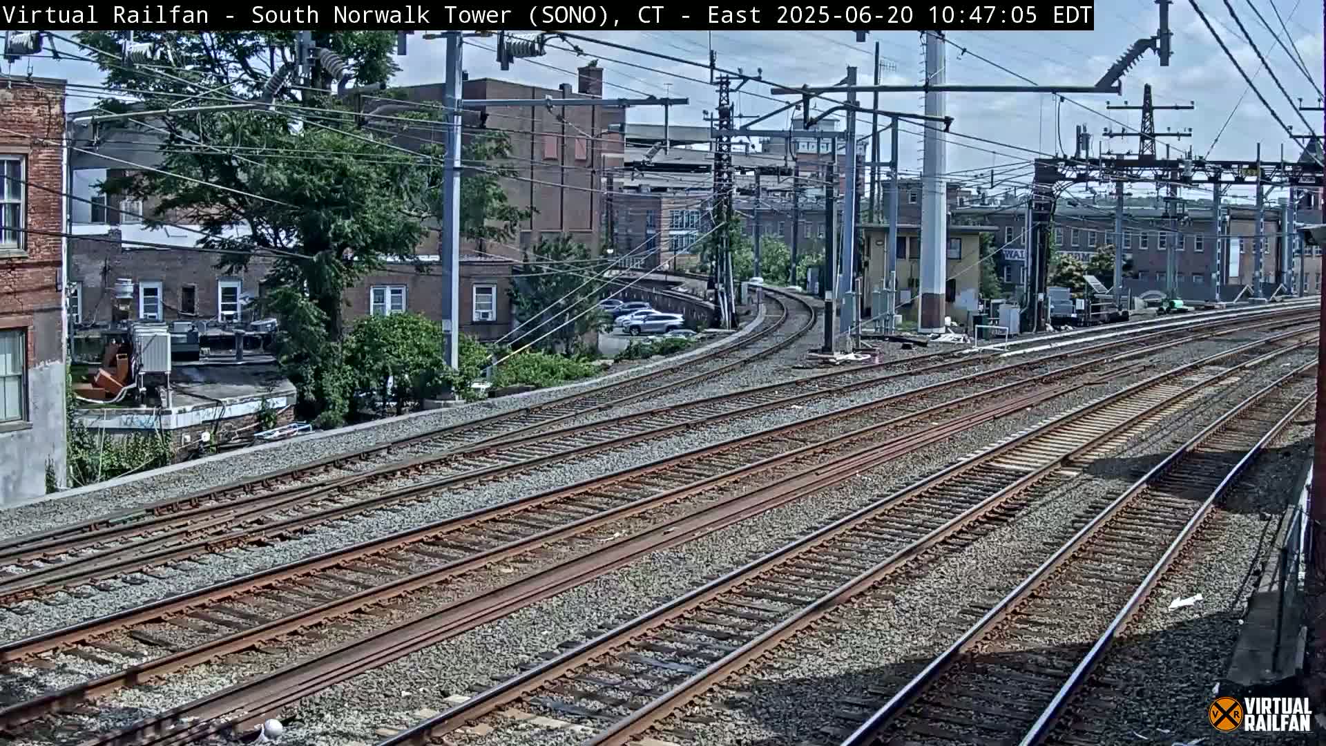 Multiple train tracks curve through a residential area on a sunny day.