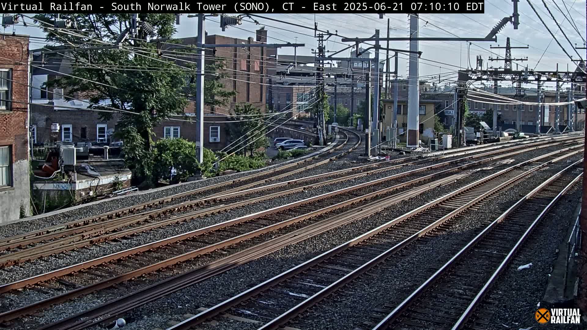 Multiple sets of train tracks curve through a city under a partly sunny sky.