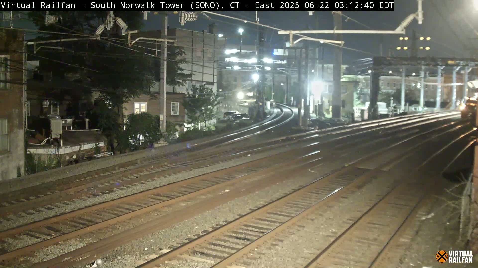 At night, multiple train tracks curve towards a distant, dimly lit urban area.