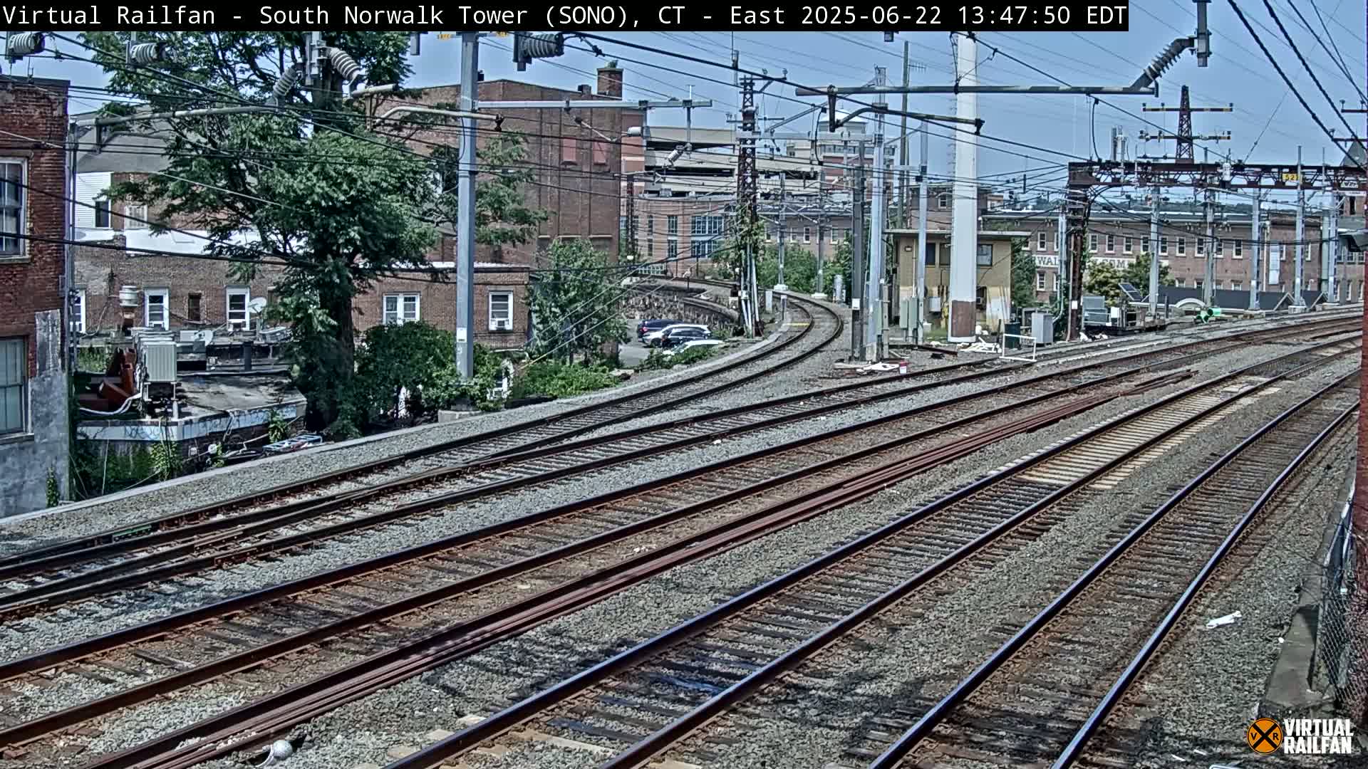 Multiple train tracks curve through an urban area under a partly sunny sky.