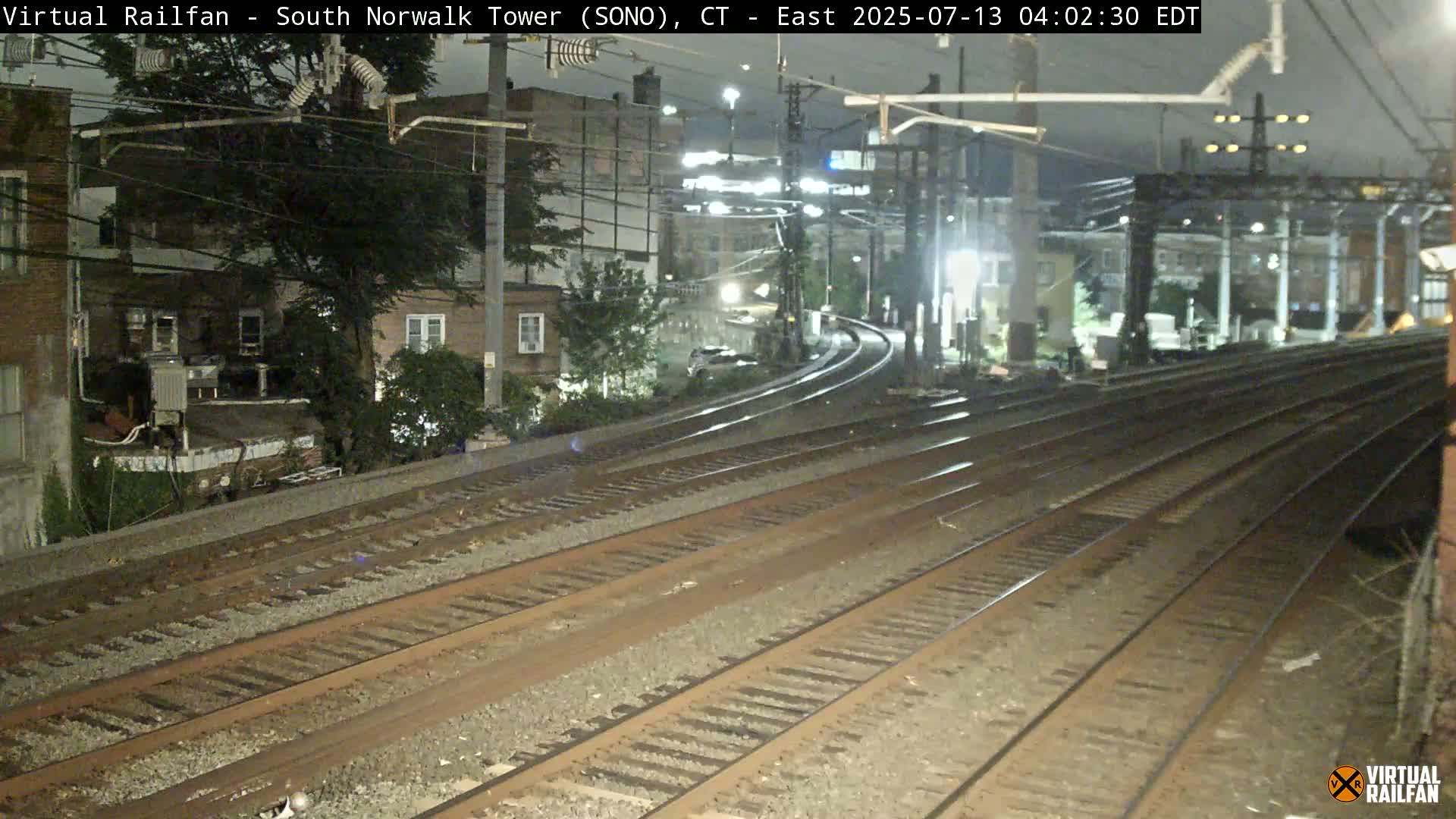 Several sets of train tracks curve around buildings under a dark, nighttime sky.