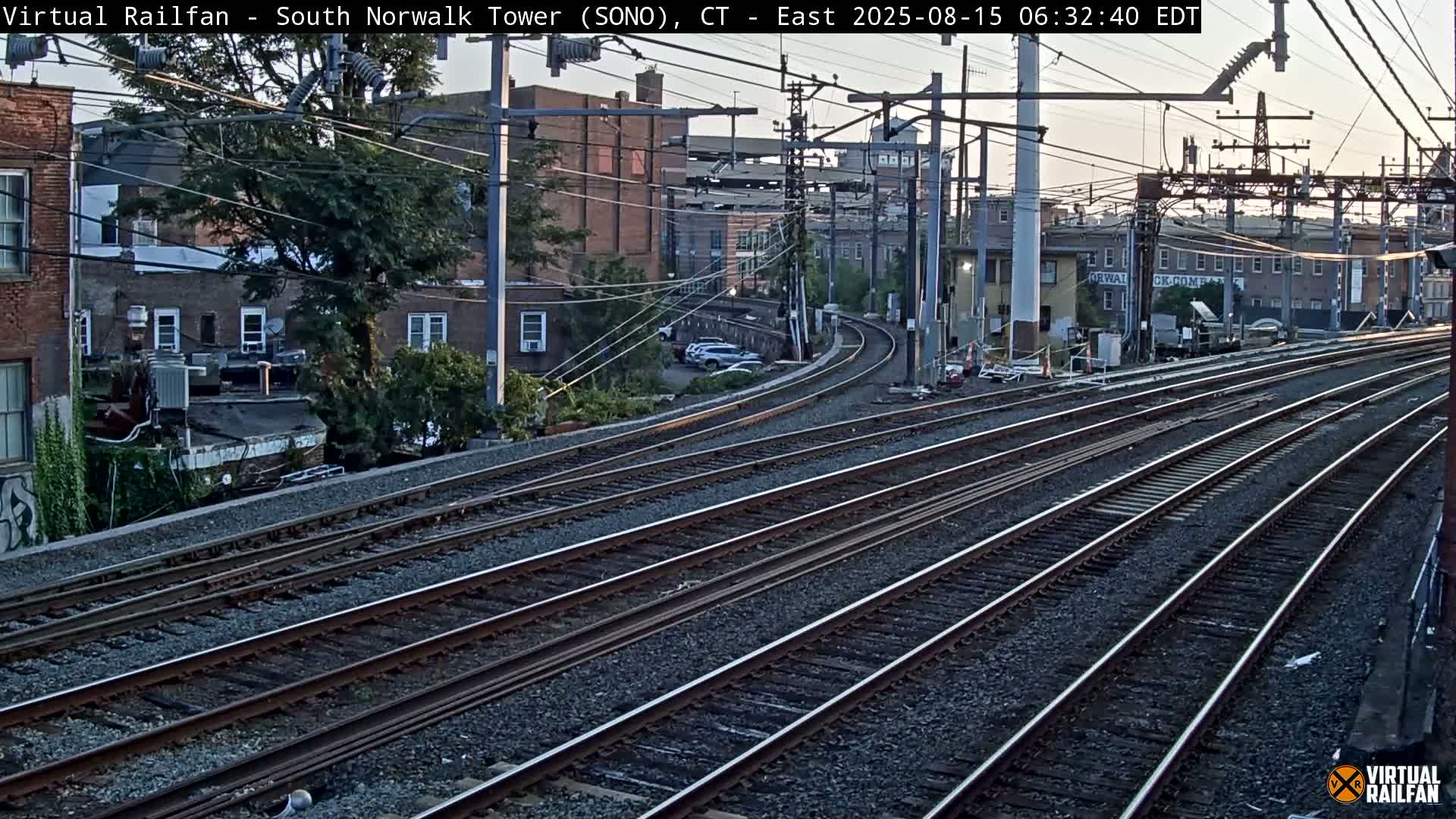 Multiple train tracks extend into the distance at night, curving slightly to the right past buildings and trees under artificial lighting.