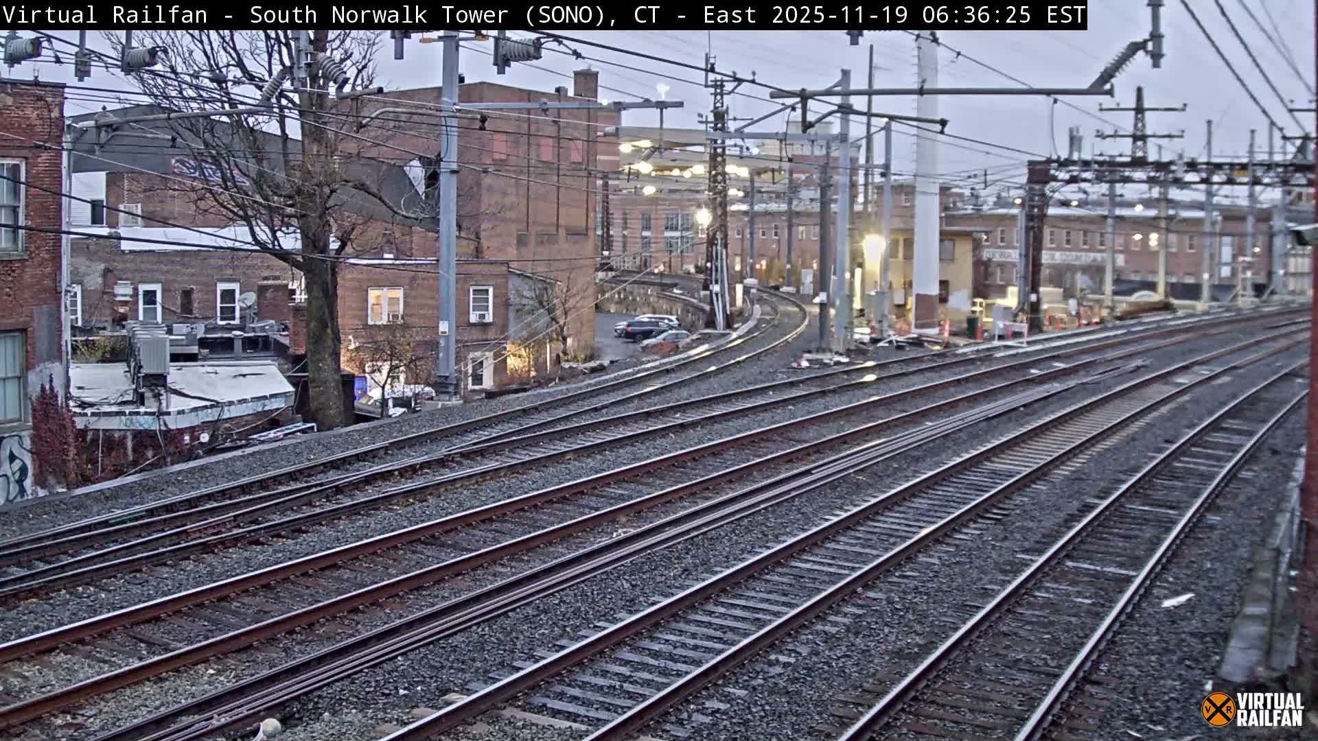Multiple train tracks extend into the distance at night, curving slightly to the right past buildings and trees under artificial lighting.