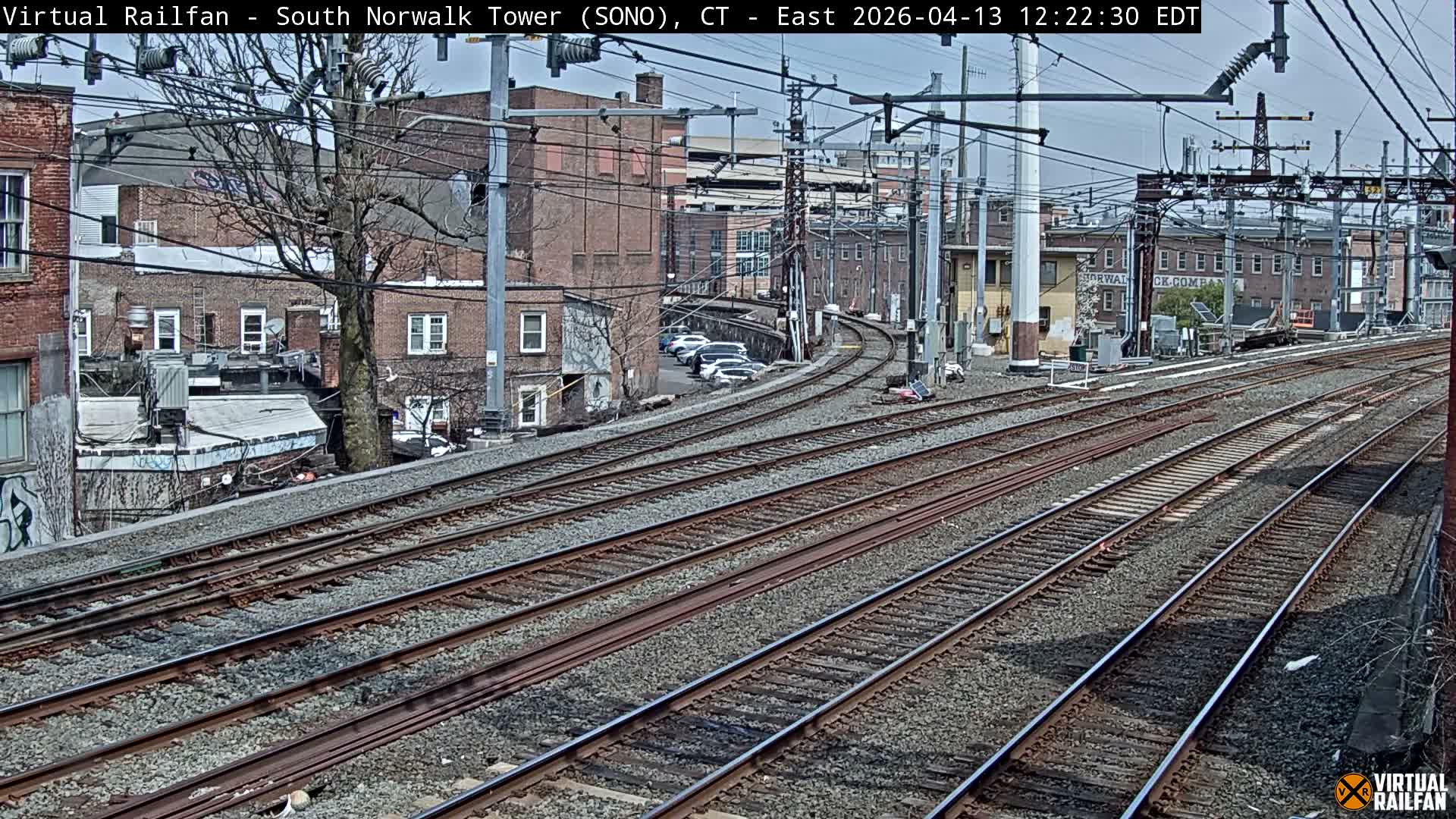 Multiple illuminated train tracks curve through an urban landscape at night, flanked by various buildings and bare trees under clear, dry conditions.
