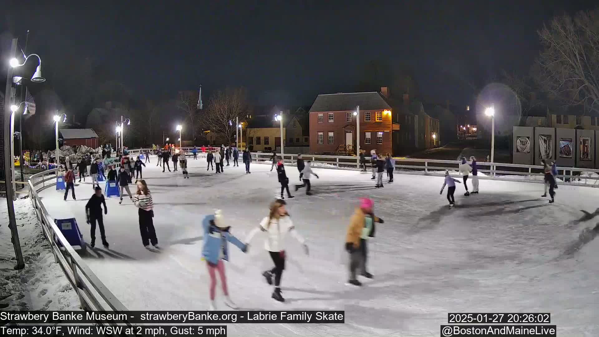 Many people ice skate on an outdoor rink at night under lights, with a 34°F temperature and a WSW wind.
