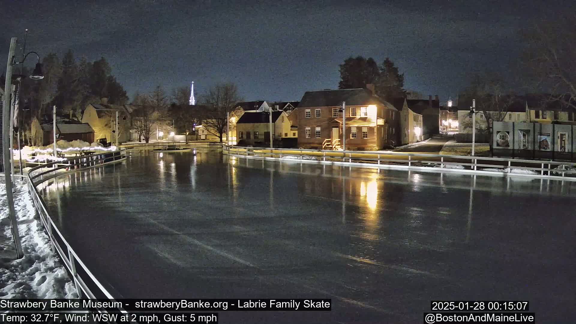 A nighttime view of an ice skating rink reflecting the lights of nearby buildings under a dark sky.